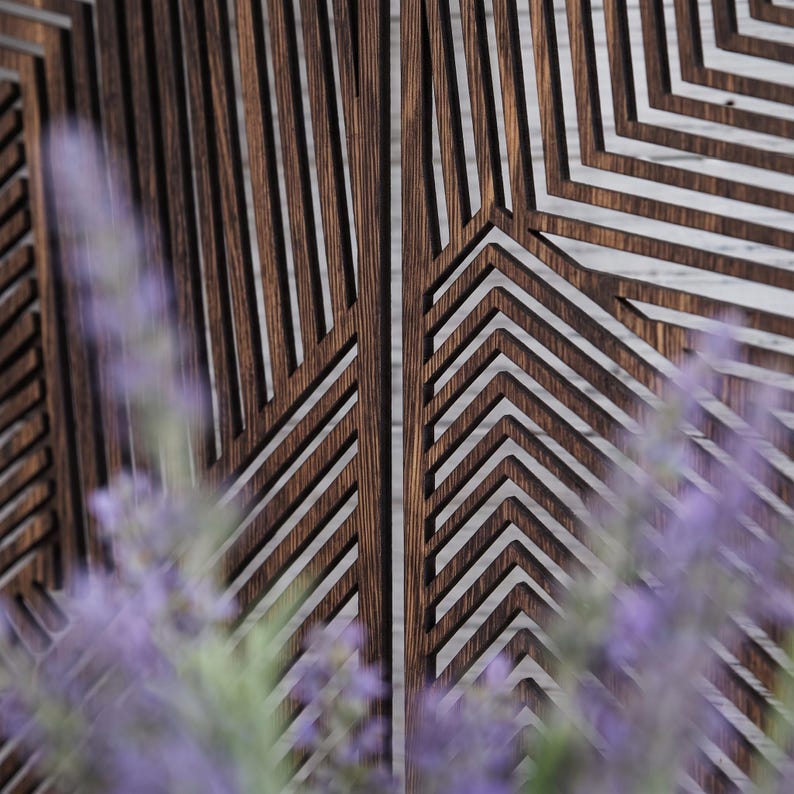 May include: A dark brown wooden wall panel featuring a series of vertical and angled slats that create a geometric pattern. The panel is composed of thin, parallel strips of wood with visible grain, arranged to form sharp, repeating chevron shapes.