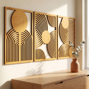 May include: Three rectangular light brown wooden wall panels featuring intricate laser-cut geometric patterns of circles and concentric arches. The panels are mounted side-by-side on a wall above a wooden surface with a small terracotta vase.