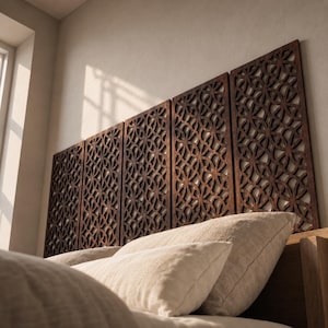 May include: Five rectangular dark brown wooden wall panels featuring an intricate laser-cut geometric pattern of overlapping circles. The panels are mounted side-by-side horizontally above a bed with light-colored pillows and bedding.