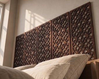 May include: Five rectangular dark brown wooden wall panels featuring an intricate laser-cut geometric pattern of overlapping circles. The panels are mounted side-by-side horizontally above a bed with light-colored pillows and bedding.