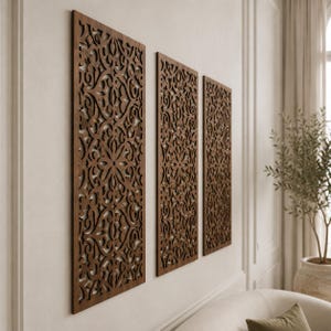 May include: Three rectangular wall panels made of dark brown wood, each featuring an intricate, laser-cut filigree pattern with symmetrical floral and scrolling motifs. The panels are mounted vertically in a row on a plain, light-colored wall.