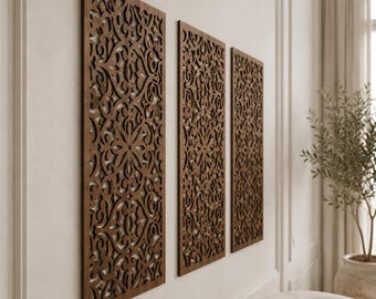 May include: Three rectangular wall panels made of dark brown wood, each featuring an intricate, laser-cut filigree pattern with symmetrical floral and scrolling motifs. The panels are mounted vertically in a row on a plain, light-colored wall.