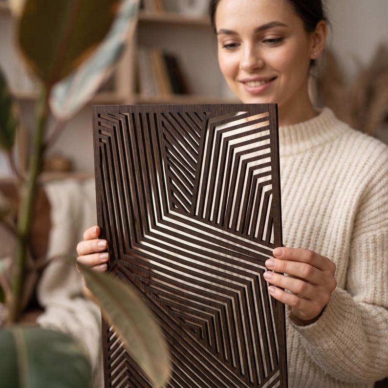 May include: A rectangular dark brown wooden wall panel featuring a laser-cut geometric pattern of parallel lines that create angular, intersecting shapes. The panel has a smooth finish and a series of open slots throughout the entire design.
