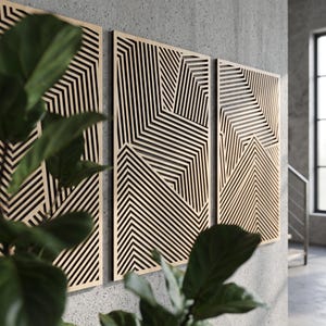 May include: A set of three rectangular wall panels featuring a light wood finish with intricate, laser-cut black geometric patterns consisting of parallel lines that create sharp, angular, and chevron-like shapes across the surface.