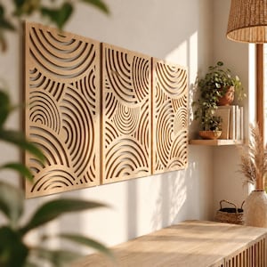 May include: A set of three rectangular light brown wooden wall panels featuring intricate laser-cut patterns of concentric semicircles and curved lines. The panels are mounted side-by-side on a plain wall, displaying a consistent geometric design.