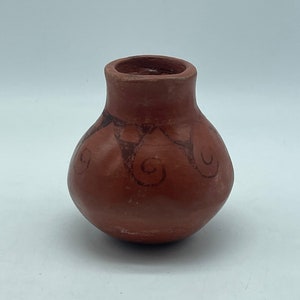 May include: A small, round, terracotta pot with a brown glaze and a decorative design of swirls. The pot is about 4 inches tall and 3 inches wide.