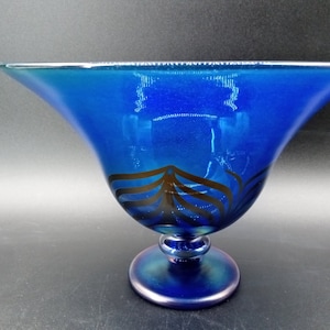 May include: A blue glass bowl with a wide, flared rim and a pedestal base. The bowl has a black and white design around the middle.