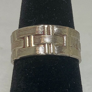 May include: A silver ring with a woven pattern. The ring is wide and has a polished finish.