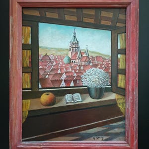 May include: An oil painting in a red frame depicts a cityscape viewed through a window. The scene includes red rooftops, a church steeple, and a vase of white flowers. An open book and an apple sit on the windowsill.