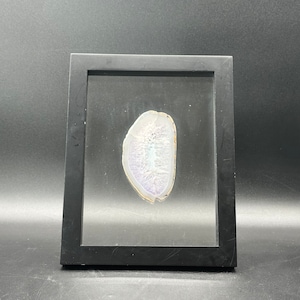 May include: A framed slice of agate with a white and purple color scheme. The agate is displayed in a black frame with a glass front.