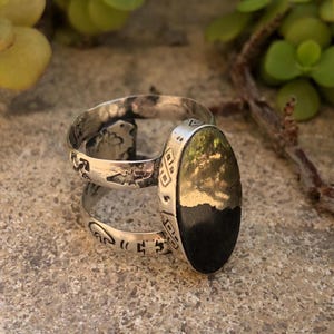 May include: A silver ring featuring a dual-band design with stamped geometric patterns and a large, oval-shaped centerpiece. The centerpiece is split horizontally, displaying a metallic gold-toned upper section and a solid black lower section.