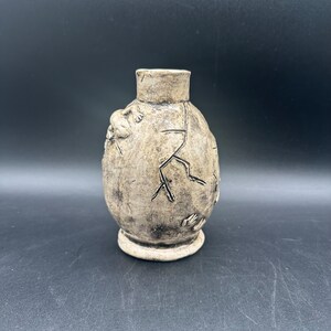 May include: A white ceramic vase with a textured surface and a crackled glaze. The vase has a round body and a narrow neck.