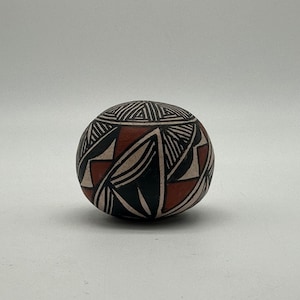 May include: A small, round, black and white pottery jar with a geometric pattern in red, white, and black. The jar is decorated with a traditional Southwestern design.