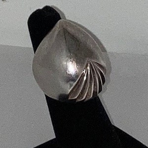 May include: A silver ring with a geometric design. The ring is shaped like a teardrop and has a series of lines radiating out from the center.