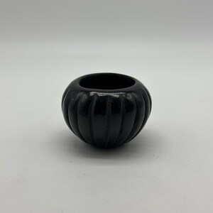 May include: A black, hand-coiled pottery bowl with a ribbed design. The bowl is round and has a smooth, glossy finish.