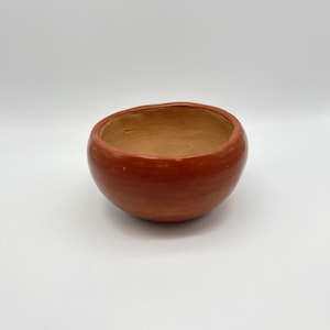 May include: A small, round, terracotta bowl with a smooth, reddish-brown glaze.