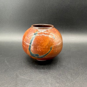 May include: A round, brown ceramic vase with a dark blue glaze. The glaze has a swirling pattern.