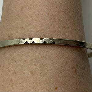 May include: A silver bangle bracelet with a textured design. The bracelet is simple and elegant.