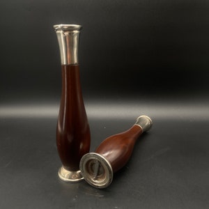 Op de afbeelding: Twee houten bloempotten met zilveren toppen. De potten zijn donkerbruin en hebben een afgeronde vorm. De zilveren toppen zijn glanzend en hebben een eenvoudig ontwerp.