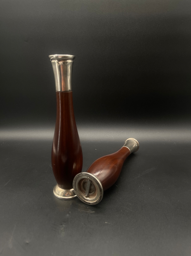 Op de afbeelding: Twee houten bloempotten met zilveren toppen. De potten zijn donkerbruin en hebben een afgeronde vorm. De zilveren toppen zijn glanzend en hebben een eenvoudig ontwerp.