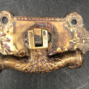 May include: Ornate antique brass drawer pull with a decorative floral design. The pull features a rectangular backplate with two mounting holes and a curved handle. The brass has a weathered, aged appearance with areas of discoloration.