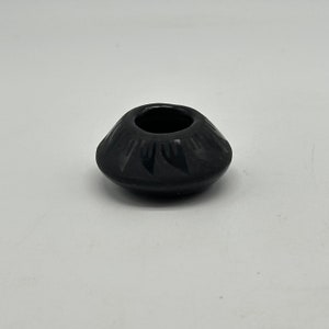 May include: A small, black, hand-painted pottery bowl with a geometric design. The bowl is about 2 inches in diameter.