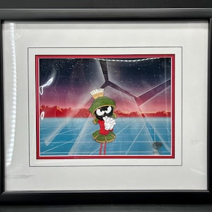 May include: Framed cartoon cel featuring Marvin the Martian. The artwork shows Marvin in his signature outfit against a futuristic, geometric background with red, blue, and purple hues. The frame is black.