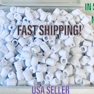May include: A close-up image of a container filled with white plastic cord ends. The container is clear plastic and the cord ends are all the same size and shape. The text "FAST SHIPPING!" is visible in the image.