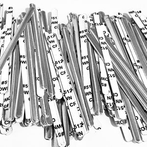 May include: A pile of silver metal nose wire strips for face masks. The strips are labeled with numbers and letters, including #5, 51, 512, WN, CF, and CRG.