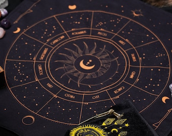 May include: Black velvet pouch with a gold drawstring and a yellow sun with a diamond in the center. The pouch is on top of a black cloth with a gold zodiac wheel with the signs of the zodiac and constellations.