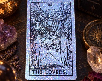 Könnte beinhalten: Eine rechteckige Tarotkarte mit holografischem Glitzereffekt und schwarzer Linienzeichnung, die Die Liebenden darstellt. Die Karte zeigt zwei Figuren unter einer großen geflügelten Engelsgestalt, mit der römischen Ziffer VI und dem Text THE LOVERS.