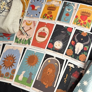 K&ouml;nnte beinhalten: Eine Sammlung von Tarotkarten mit dem Narren, der K&ouml;nigin der M&uuml;nzen, der Hohenpriesterin, der Herrscherin, den Liebenden, dem Hierophanten, dem Herrscher, dem Tod, dem Teufel, der Sonne, dem Mond und der Kraft sowie einem beigen Beutel.