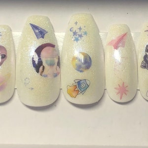 Puede incluir: Conjunto de 10 uñas postizas blancas con temática espacial. Las uñas presentan varios diseños con temática espacial, incluyendo planetas, estrellas, naves espaciales y extraterrestres.