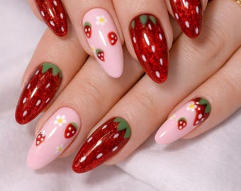 May include: A set of almond-shaped artificial nails with a strawberry design. Some nails are painted a vibrant red with white speckles and green tips, while others are light pink with small strawberry and flower designs.