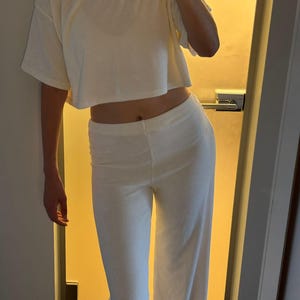 Pu&ograve; includere: Completo da relax color crema composto da due pezzi. Il set include una t-shirt corta a maniche corte e pantaloni a gamba larga. Il tessuto sembra essere un materiale morbido e strutturato. L'outfit &egrave; semplice e confortevole.