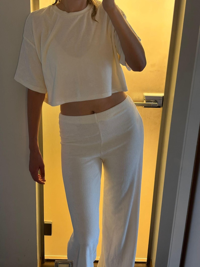 Pu&ograve; includere: Completo da relax color crema composto da due pezzi. Il set include una t-shirt corta a maniche corte e pantaloni a gamba larga. Il tessuto sembra essere un materiale morbido e strutturato. L'outfit &egrave; semplice e confortevole.