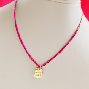 May include: A pink string necklace with a gold charm that says "Good Luck".