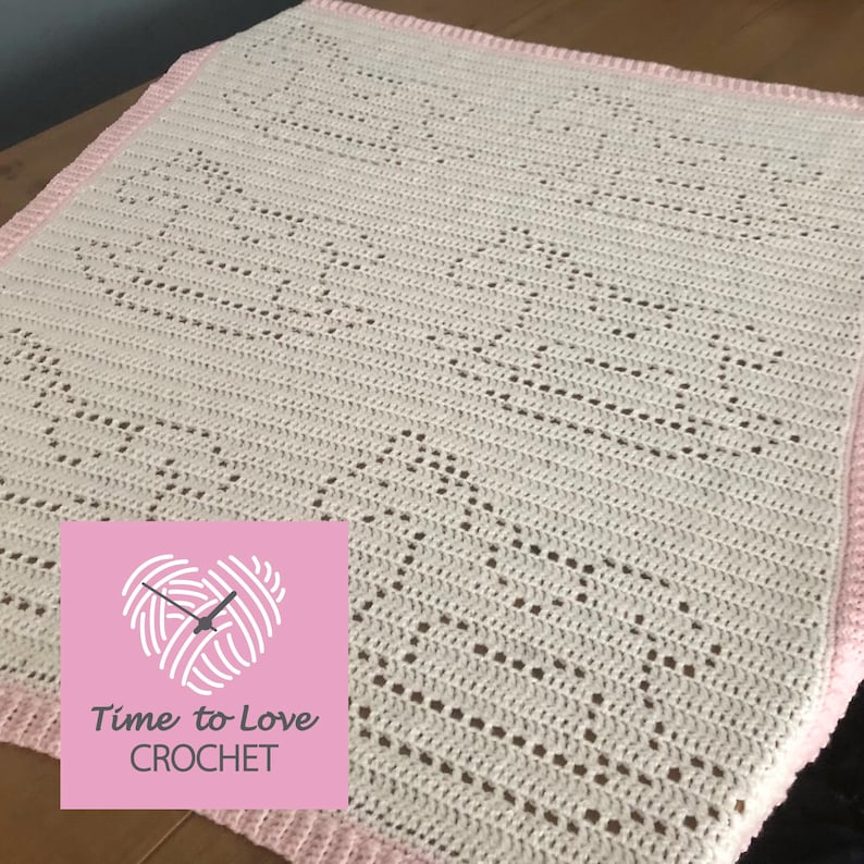 Puede incluir: Una manta de beb&eacute; de crochet blanco con un borde rosa y un patr&oacute;n de coraz&oacute;n repetitivo. La manta est&aacute; hecha con un punto abierto delicado y tiene una sensaci&oacute;n suave y aireada. La manta est&aacute; etiquetada "Time to Love Crochet".