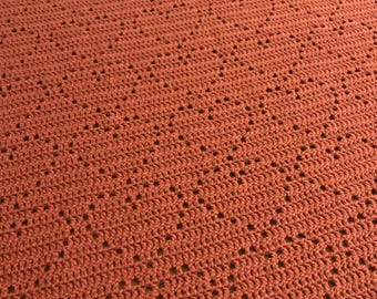 May include: A close-up of a crocheted blanket with a diamond pattern in a burnt orange color.