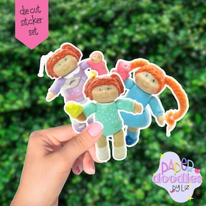 May include: A die-cut sticker set featuring three Cabbage Patch Kids dolls. One doll wears a blue dress, another a purple outfit, and the third a green outfit and holds an ice cream cone. The stickers have a white border and are set against a green background.