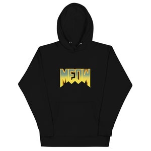 Pu&ograve; includere: Felpa con cappuccio nera con una grafica "MEOW" gialla e blu in uno stile di font da videogioco retr&ograve;.