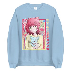 May include: A light blue sweatshirt with a graphic of a pink-haired anime girl holding a blue cat. The graphic is surrounded by a yellow and pink frame with stars and the text "ネコと かわいい" in Japanese.
