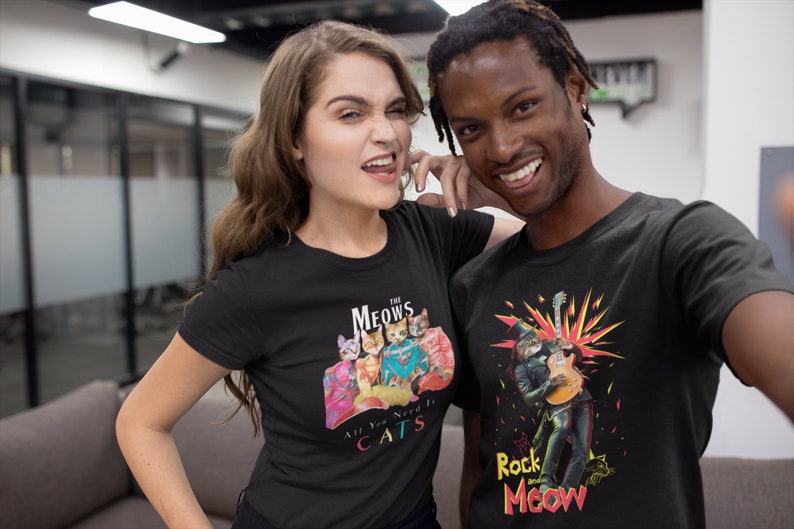 K&ouml;nnte beinhalten: Zwei Personen tragen schwarze T-Shirts mit Katzenmotiven. Das Shirt der Frau zeigt eine Katzenband namens "The Meows" mit dem Text "All You Need Is Cats". Das Shirt des Mannes zeigt eine Katze, die als Rockstar verkleidet ist, mit dem Text "Rock and Meow".