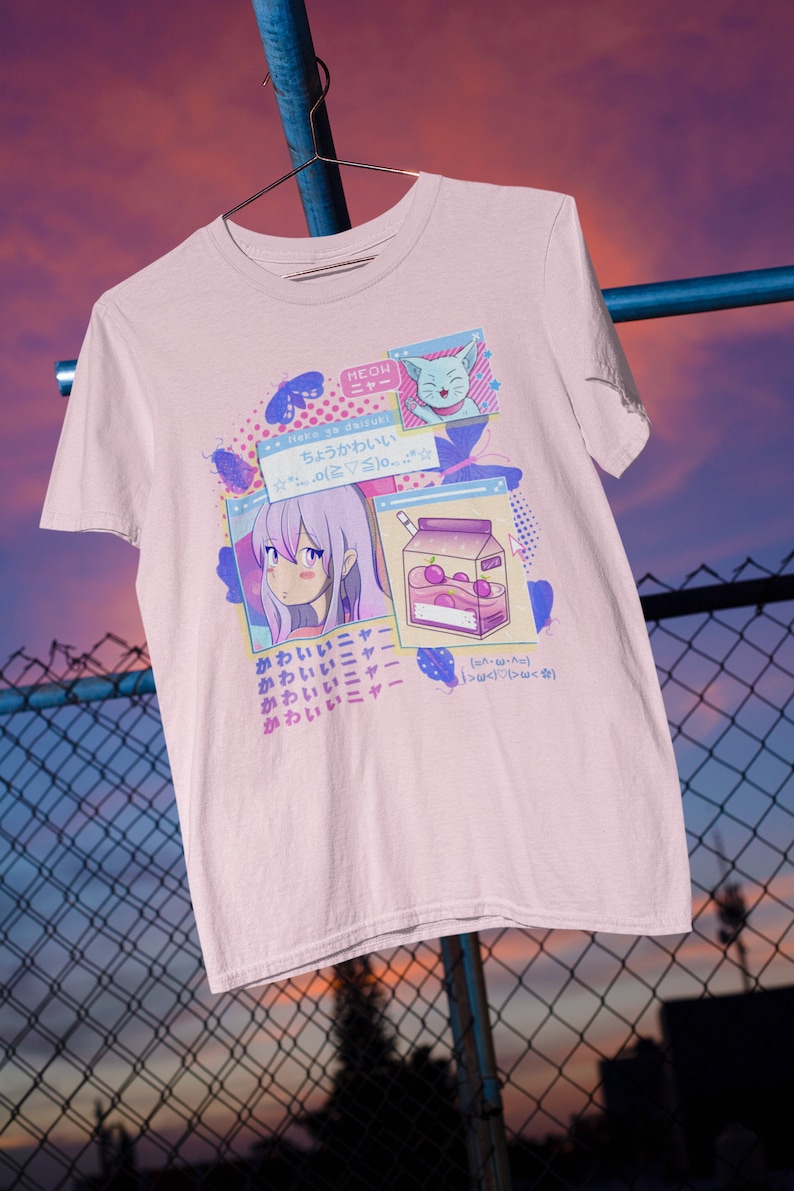 Pu&ograve; includere: Una maglietta rosa con un design grafico che presenta una ragazza dei cartoni animati con i capelli viola, un gatto e una scatola di succo. Il testo sulla maglietta recita "Neko ga daizuki" e "chou kawaii".