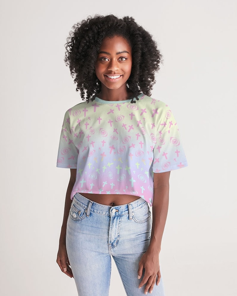May include: A cropped t-shirt with a pastel pink, blue and yellow ombre design. The shirt features a repeating pattern of pink crosses and white swirls.