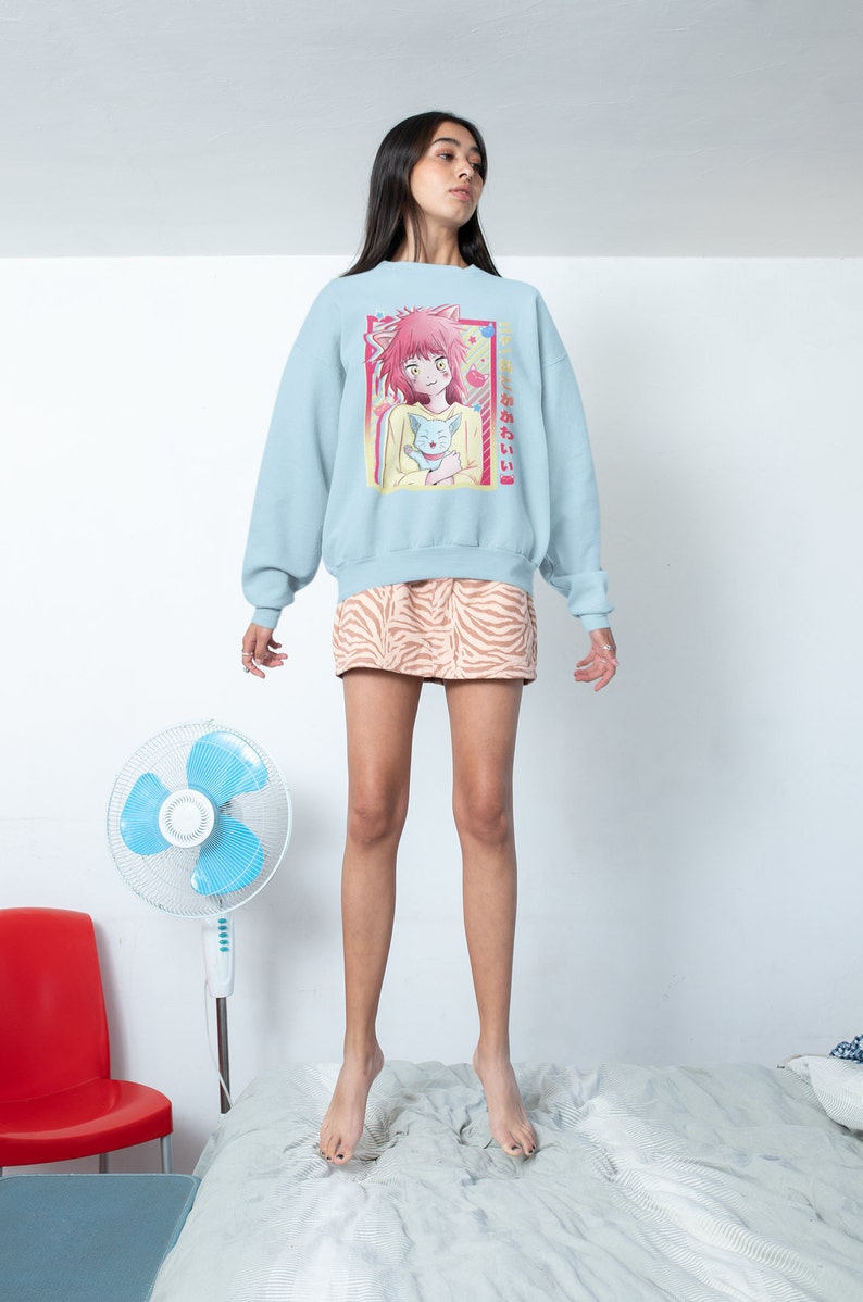 May include: A light blue sweatshirt with a graphic print of an anime character holding a cat. The text on the sweatshirt says "きみとあいたい".