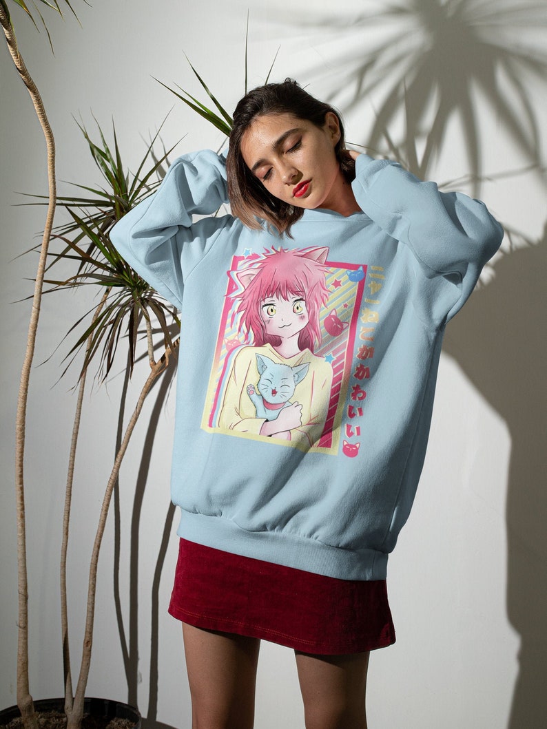 May include: A light blue sweatshirt with a graphic print of a pink-haired anime character holding a blue cat. The text "ねこがあいたい" is printed on the right side of the graphic.