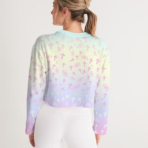May include: A pastel pink, yellow and blue ombre cropped sweatshirt with a pattern of pink crosses and eyes. The sweatshirt has long sleeves and a relaxed fit.