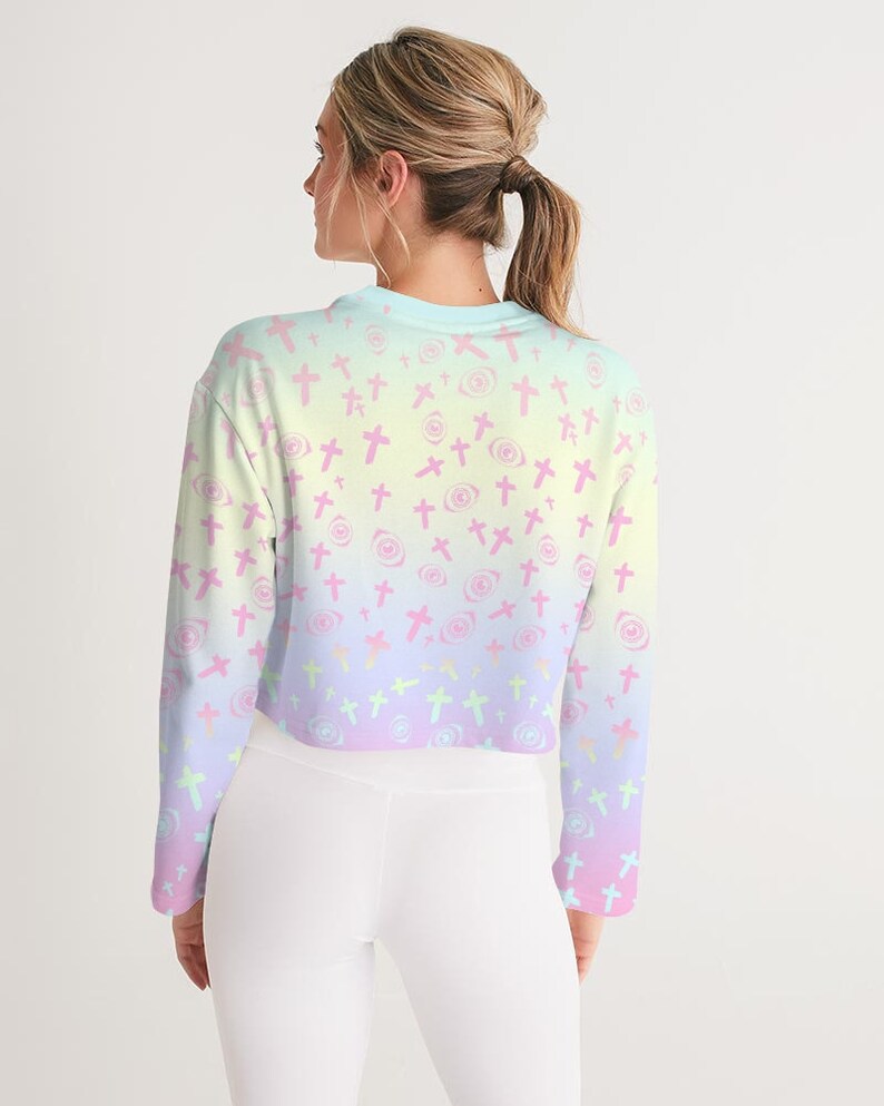 May include: A pastel pink, yellow and blue ombre cropped sweatshirt with a pattern of pink crosses and eyes. The sweatshirt has long sleeves and a relaxed fit.