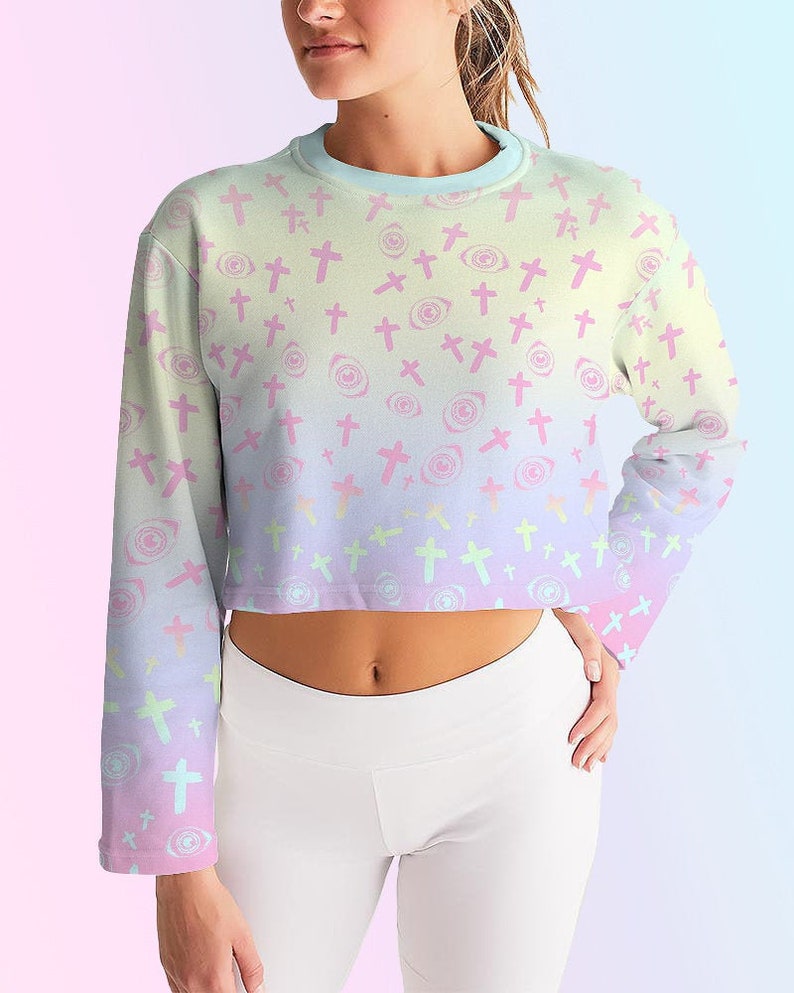 May include: A pastel pink, blue and yellow ombre cropped sweatshirt with a repeating pattern of pink crosses and eyes.